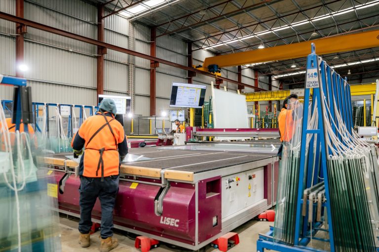Wide view of operators and automated glass cutting equipment in the Tough Glass factory.