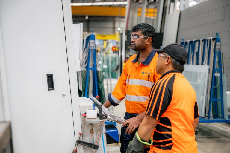 Tough Glass operators reviewing production at a machine control panel.